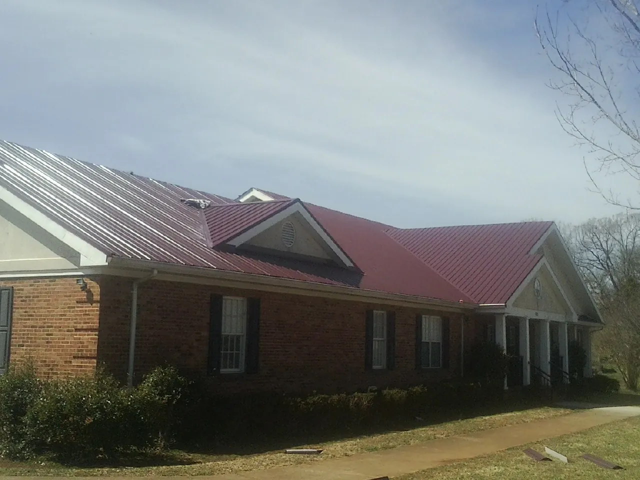 Red metal roof with gabled entries on a long brick building, from a Hail Damage Roof Repair job in Van Wert