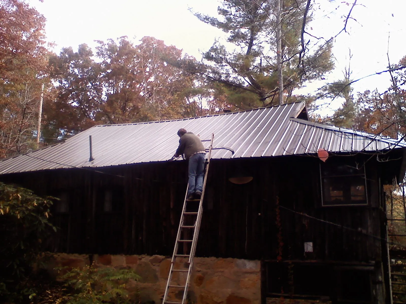 Roofer on a ladder working along the edge of a cabin metal roof in Van Wert