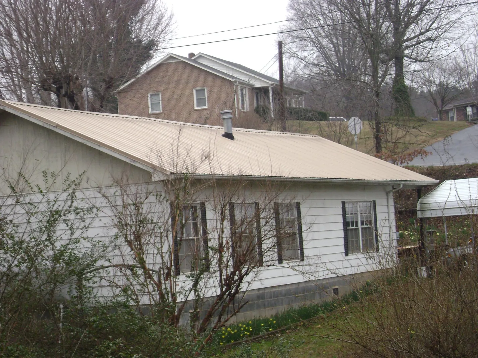 Tan metal roof on a white sided house set into a hillside — Commercial Roofing by Roofing Brothers in Van Wert