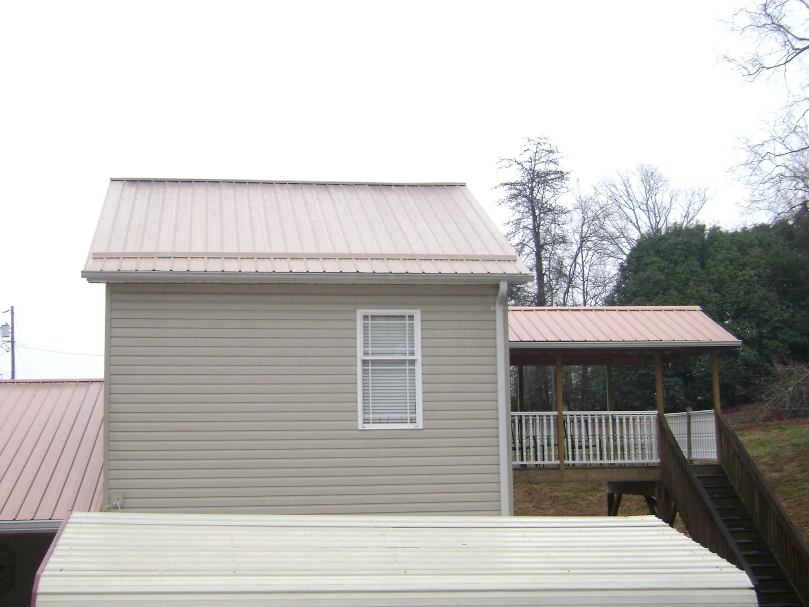 Tan metal roofs on a two story addition and attached porch, from a Roof Replacement job in Van Wert